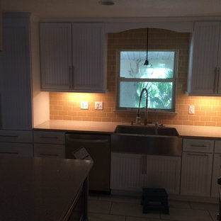 This is an example of a mid-sized beach style l-shaped eat-in kitchen in Orlando with a farmhouse sink, louvered cabinets, green cabinets, quartz benchtops, yellow splashback, subway tile splashback, stainless steel appliances, porcelain floors and with island.