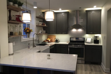 Eat-in kitchen - small transitional u-shaped light wood floor eat-in kitchen idea in Cincinnati with a farmhouse sink, raised-panel cabinets, gray cabinets, quartz countertops, gray backsplash, glass tile backsplash, stainless steel appliances and a peninsula