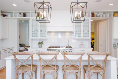 Example of a large country l-shaped light wood floor eat-in kitchen design in Chicago with a farmhouse sink, shaker cabinets, white cabinets, marble countertops, white backsplash, subway tile backsplash, stainless steel appliances and an island