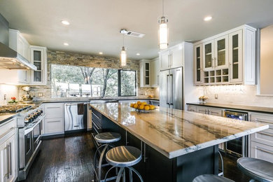 Example of a mid-sized trendy u-shaped dark wood floor and brown floor kitchen design in Dallas with a farmhouse sink, stainless steel appliances, white backsplash, stone tile backsplash, shaker cabinets, white cabinets, quartzite countertops and an island