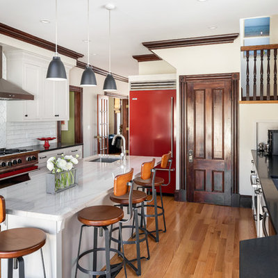 Large transitional galley medium tone wood floor and brown floor kitchen photo in Boston with ceramic backsplash, an island, an undermount sink, shaker cabinets, white cabinets, white backsplash and black countertops