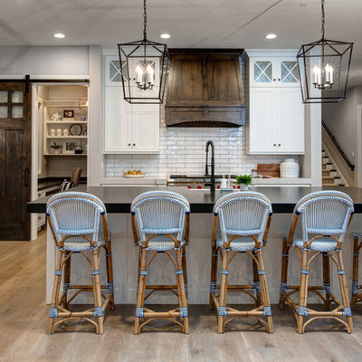 Large country single-wall medium tone wood floor open concept kitchen photo in Salt Lake City with a farmhouse sink, shaker cabinets, white cabinets, white backsplash, subway tile backsplash, stainless steel appliances, an island, soapstone countertops and black countertops