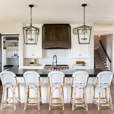 Inspiration for a large farmhouse single-wall medium tone wood floor open concept kitchen remodel in Salt Lake City with a farmhouse sink, white cabinets, white backsplash, subway tile backsplash, an island, shaker cabinets, soapstone countertops, stainless steel appliances and black countertops