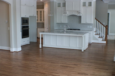 Mid-sized elegant l-shaped medium tone wood floor and brown floor eat-in kitchen photo in Raleigh with an island, a single-bowl sink, shaker cabinets, white cabinets, granite countertops, gray backsplash and ceramic backsplash