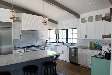 Large country l-shaped medium tone wood floor and brown floor kitchen photo in Other with a farmhouse sink, shaker cabinets, white cabinets, marble countertops, gray backsplash, subway tile backsplash, stainless steel appliances and an island