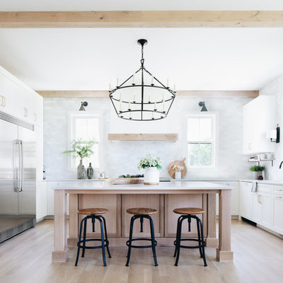 Farmhouse u-shaped light wood floor and beige floor eat-in kitchen photo in Chicago with an undermount sink, shaker cabinets, white cabinets, gray backsplash, stainless steel appliances, an island and white countertops