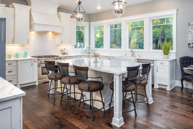 Large elegant dark wood floor kitchen photo in Other with a farmhouse sink, shaker cabinets, white cabinets, quartzite countertops, white backsplash, subway tile backsplash, stainless steel appliances, an island and white countertops