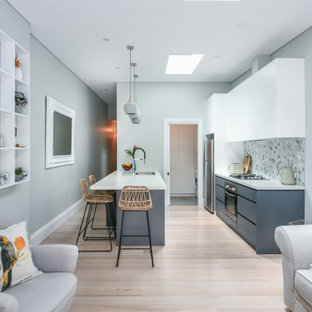 Mid-sized contemporary galley open plan kitchen in Sydney with an undermount sink, flat-panel cabinets, white cabinets, quartz benchtops, multi-coloured splashback, mosaic tile splashback, stainless steel appliances, light hardwood floors, a peninsula, brown floor and white benchtop.
