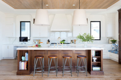 Foto de cocina costera con armarios estilo shaker, puertas de armario blancas, salpicadero blanco, suelo de madera en tonos medios y una isla