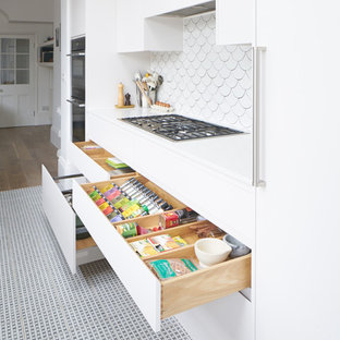 Design ideas for a large contemporary galley separate kitchen in London with an integrated sink, white cabinets, white splashback, stainless steel appliances, porcelain floors and no island.