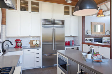 Enclosed kitchen - mid-sized eclectic l-shaped medium tone wood floor and brown floor enclosed kitchen idea in San Francisco with a farmhouse sink, shaker cabinets, white cabinets, solid surface countertops, white backsplash, subway tile backsplash, stainless steel appliances, an island and gray countertops