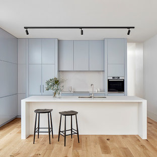 Inspiration for a small modern galley kitchen in Melbourne with a double-bowl sink, flat-panel cabinets, blue cabinets, white splashback, light hardwood floors, with island, white benchtop, panelled appliances and beige floor.
