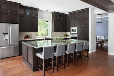 Example of a large urban single-wall medium tone wood floor and brown floor eat-in kitchen design in Austin with a farmhouse sink, shaker cabinets, dark wood cabinets, granite countertops, beige backsplash, porcelain backsplash, stainless steel appliances, an island and green countertops