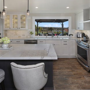 Inspiration for a mid-sized eclectic l-shaped open plan kitchen in Orange County with an undermount sink, recessed-panel cabinets, white cabinets, quartz benchtops, grey splashback, marble splashback, stainless steel appliances, porcelain floors, with island, brown floor and white benchtop.