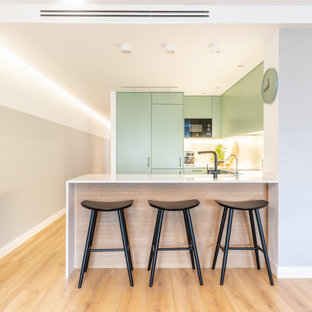 Imagen de cocina en U, escandinava, con armarios con paneles lisos, puertas de armario verdes, electrodomésticos con paneles, suelo de madera clara, península, suelo beige y encimeras blancas