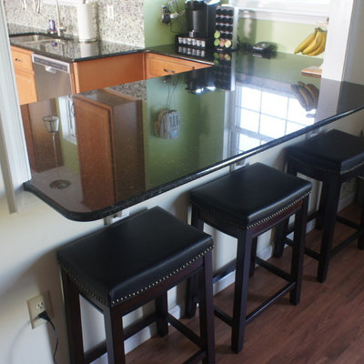 Example of a small trendy u-shaped linoleum floor eat-in kitchen design in Baltimore with an undermount sink, raised-panel cabinets, medium tone wood cabinets, granite countertops, green backsplash, glass tile backsplash, stainless steel appliances and a peninsula