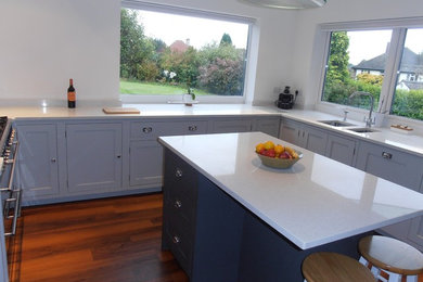 This is an example of a medium sized contemporary l-shaped open plan kitchen in Hampshire with a submerged sink, shaker cabinets, grey cabinets, quartz worktops, white splashback, glass sheet splashback, stainless steel appliances, lino flooring and an island.