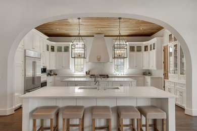 Photo of an expansive farmhouse u-shaped open plan kitchen in Miami with a submerged sink, shaker cabinets, white cabinets, engineered stone countertops, white splashback, stone slab splashback, stainless steel appliances, medium hardwood flooring and multiple islands.
