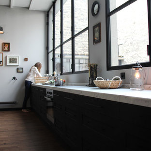 Ejemplo de cocina lineal, retro, grande, abierta, con puertas de armario negras, encimera de mármol, salpicadero blanco, electrodomésticos con paneles y suelo de madera oscura