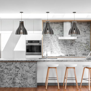Inspiration for a contemporary galley open plan kitchen in Hobart with white cabinets, granite benchtops, stainless steel appliances, grey benchtop, flat-panel cabinets, grey splashback, medium hardwood floors, with island and brown floor.