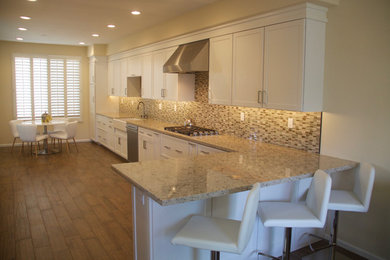 Transitional l-shaped porcelain tile eat-in kitchen photo in Orange County with a farmhouse sink, shaker cabinets, white cabinets, quartz countertops, multicolored backsplash, mosaic tile backsplash and stainless steel appliances