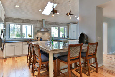 Inspiration for a mid-sized coastal l-shaped light wood floor eat-in kitchen remodel in Milwaukee with an undermount sink, flat-panel cabinets, white cabinets, granite countertops, beige backsplash, porcelain backsplash, stainless steel appliances and an island