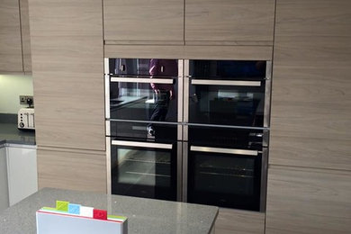 This is an example of a large contemporary l-shaped open plan kitchen in West Midlands with flat-panel cabinets, quartz worktops, stainless steel appliances, a double-bowl sink, ceramic flooring, grey cabinets and a breakfast bar.