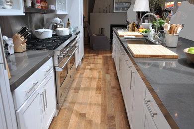 Large transitional galley light wood floor and brown floor kitchen photo in Chicago with an undermount sink, flat-panel cabinets, white cabinets, concrete countertops, stainless steel appliances and an island