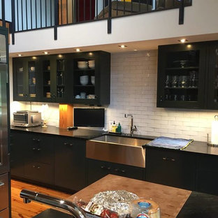 Design ideas for a mid-sized shabby-chic style eat-in kitchen in Denver with a farmhouse sink, flat-panel cabinets, black cabinets, soapstone benchtops, white splashback, stainless steel appliances, medium hardwood floors and with island.