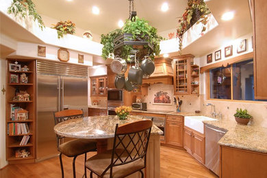 Inredning av ett medelhavsstil stort kök, med en rustik diskho, luckor med upphöjd panel, skåp i ljust trä, granitbänkskiva, beige stänkskydd, stänkskydd i stenkakel, rostfria vitvaror, ljust trägolv och en köksö