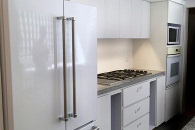 マイアミにある小さなトラディショナルスタイルのおしゃれな独立型キッチン (フラットパネル扉のキャビネット、白いキャビネット、白い調理設備、グレーの床、グレーのキッチンカウンター) の写真