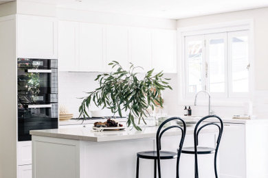 シドニーにある中くらいなトランジショナルスタイルのおしゃれなキッチン (シェーカースタイル扉のキャビネット、白いキャビネット、白いキッチンパネル、無垢フローリング、茶色い床、白いキッチンカウンター、窓) の写真