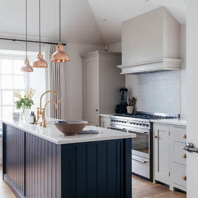 Kitchen - mid-sized coastal galley medium tone wood floor and brown floor kitchen idea in Cornwall with a farmhouse sink, gray cabinets, solid surface countertops, blue backsplash, ceramic backsplash, stainless steel appliances, an island and white countertops