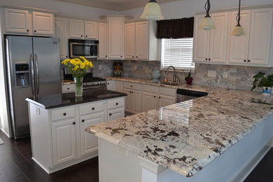 Example of a mid-sized classic u-shaped laminate floor and brown floor enclosed kitchen design in New Orleans with an undermount sink, raised-panel cabinets, white cabinets, granite countertops, beige backsplash, stone tile backsplash, stainless steel appliances and an island
