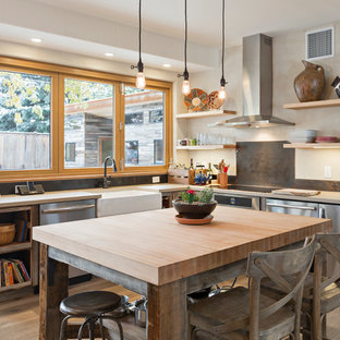 Inspiration pour une cuisine américaine sud-ouest américain en U de taille moyenne avec un évier de ferme, un placard sans porte, des portes de placard en bois vieilli, un plan de travail en quartz modifié, une crédence métallisée, un électroménager en acier inoxydable, un sol en bois clair, un îlot central, un sol beige et un plan de travail gris.