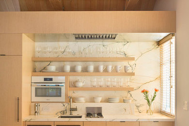 サンフランシスコにある小さなコンテンポラリースタイルのおしゃれなダイニングキッチン (シングルシンク、フラットパネル扉のキャビネット、シルバーの調理設備、淡色木目調キャビネット、大理石カウンター、白いキッチンパネル) の写真