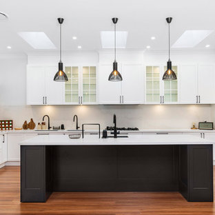Inspiration pour une grand cuisine américaine traditionnelle en U avec un évier encastré, un placard à porte shaker, des portes de placard jaunes, un plan de travail en quartz modifié, une crédence blanche, une crédence en quartz modifié, un électroménager en acier inoxydable, un sol en bois brun, un îlot central, un sol marron et un plan de travail blanc.