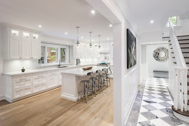 Eat-in kitchen - large transitional l-shaped light wood floor eat-in kitchen idea in Toronto with an undermount sink, shaker cabinets, white cabinets, marble countertops, white backsplash, marble backsplash, paneled appliances and an island