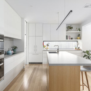 Photo of a contemporary l-shaped kitchen in Melbourne with an undermount sink, flat-panel cabinets, white cabinets, grey splashback, black appliances, light hardwood floors, with island, beige floor and white benchtop.
