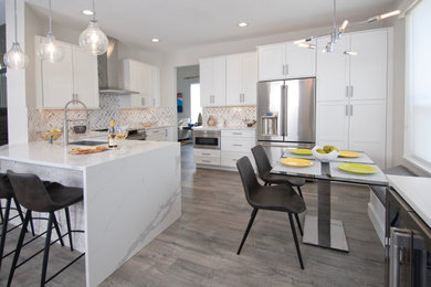 Example of a mid-sized minimalist l-shaped laminate floor and gray floor open concept kitchen design in Miami with an undermount sink, shaker cabinets, white cabinets, quartz countertops, gray backsplash, ceramic backsplash, stainless steel appliances and white countertops