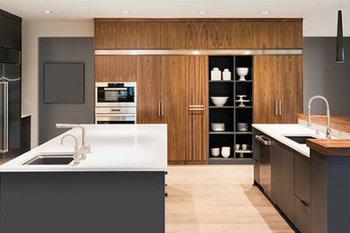 Kitchen - huge contemporary l-shaped light wood floor and beige floor kitchen idea in Other with an undermount sink, flat-panel cabinets, dark wood cabinets, solid surface countertops, paneled appliances, two islands and white countertops