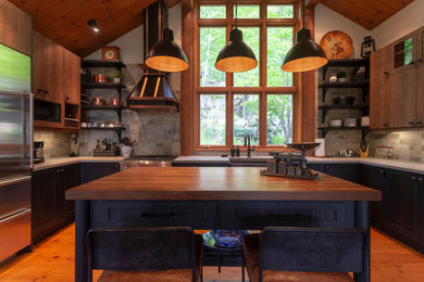 Inspiration for a mid-sized rustic u-shaped medium tone wood floor and orange floor eat-in kitchen remodel in Montreal with a farmhouse sink, flat-panel cabinets, medium tone wood cabinets, concrete countertops, gray backsplash, stone tile backsplash, stainless steel appliances, an island and gray countertops