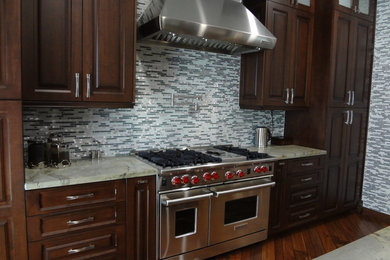 Example of a classic l-shaped eat-in kitchen design in Los Angeles with raised-panel cabinets, dark wood cabinets, marble countertops, white backsplash, stone tile backsplash and stainless steel appliances