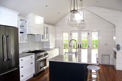 Example of a large beach style single-wall medium tone wood floor and brown floor kitchen design in Boston with an undermount sink, shaker cabinets, white cabinets, quartz countertops, white backsplash, marble backsplash, stainless steel appliances and an island