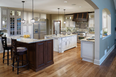 Eat-in kitchen - mid-sized traditional l-shaped light wood floor eat-in kitchen idea in Chicago with glass-front cabinets, two islands, white cabinets, granite countertops, multicolored backsplash, stone tile backsplash and stainless steel appliances