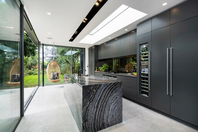 Photo of a contemporary galley kitchen in London with a submerged sink, flat-panel cabinets, black cabinets, black splashback, glass sheet splashback, stainless steel appliances, concrete flooring and an island.