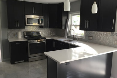 Large transitional u-shaped marble floor and gray floor eat-in kitchen photo in New York with an undermount sink, recessed-panel cabinets, black cabinets, solid surface countertops, metallic backsplash, mosaic tile backsplash, stainless steel appliances, a peninsula and white countertops
