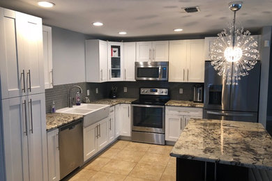 Photo of a medium sized contemporary l-shaped enclosed kitchen in Orlando with a belfast sink, shaker cabinets, white cabinets, granite worktops, grey splashback, mosaic tiled splashback, stainless steel appliances, travertine flooring, an island, beige floors and beige worktops.