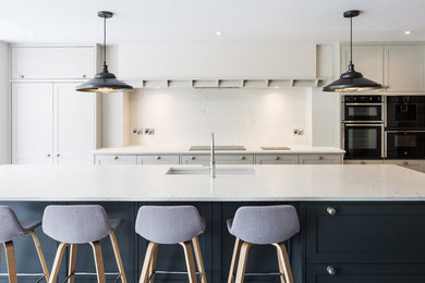 Inspiration for an expansive classic open plan kitchen in Cheshire with grey cabinets, an island, a submerged sink, shaker cabinets, white splashback, black appliances and white worktops.