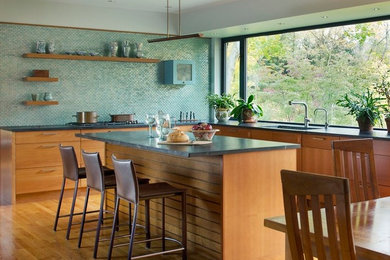 Bild på ett vintage grå grått kök, med en undermonterad diskho, släta luckor, skåp i mellenmörkt trä, bänkskiva i täljsten, blått stänkskydd, stänkskydd i glaskakel, integrerade vitvaror, mellanmörkt trägolv, en köksö och brunt golv